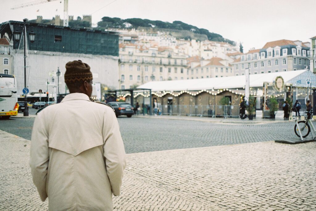 A man in a trench coat in Lisbon's cityscape, showcasing urban fashion.